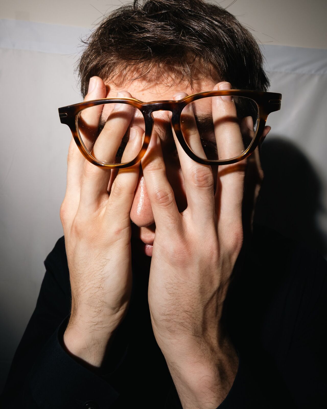 Cameron holding his glasses against his face with both hands